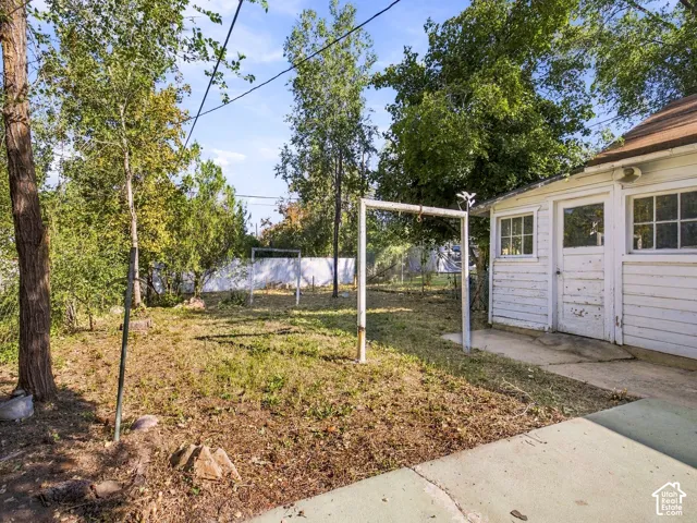 Exterior space featuring mature trees, a concrete patio, wood-siding finish, and a white privacy fence