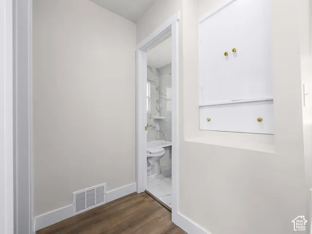 Recessed built-in cabinetry featuring white doors and brass-finish hardware, paired with wood-finish flooring