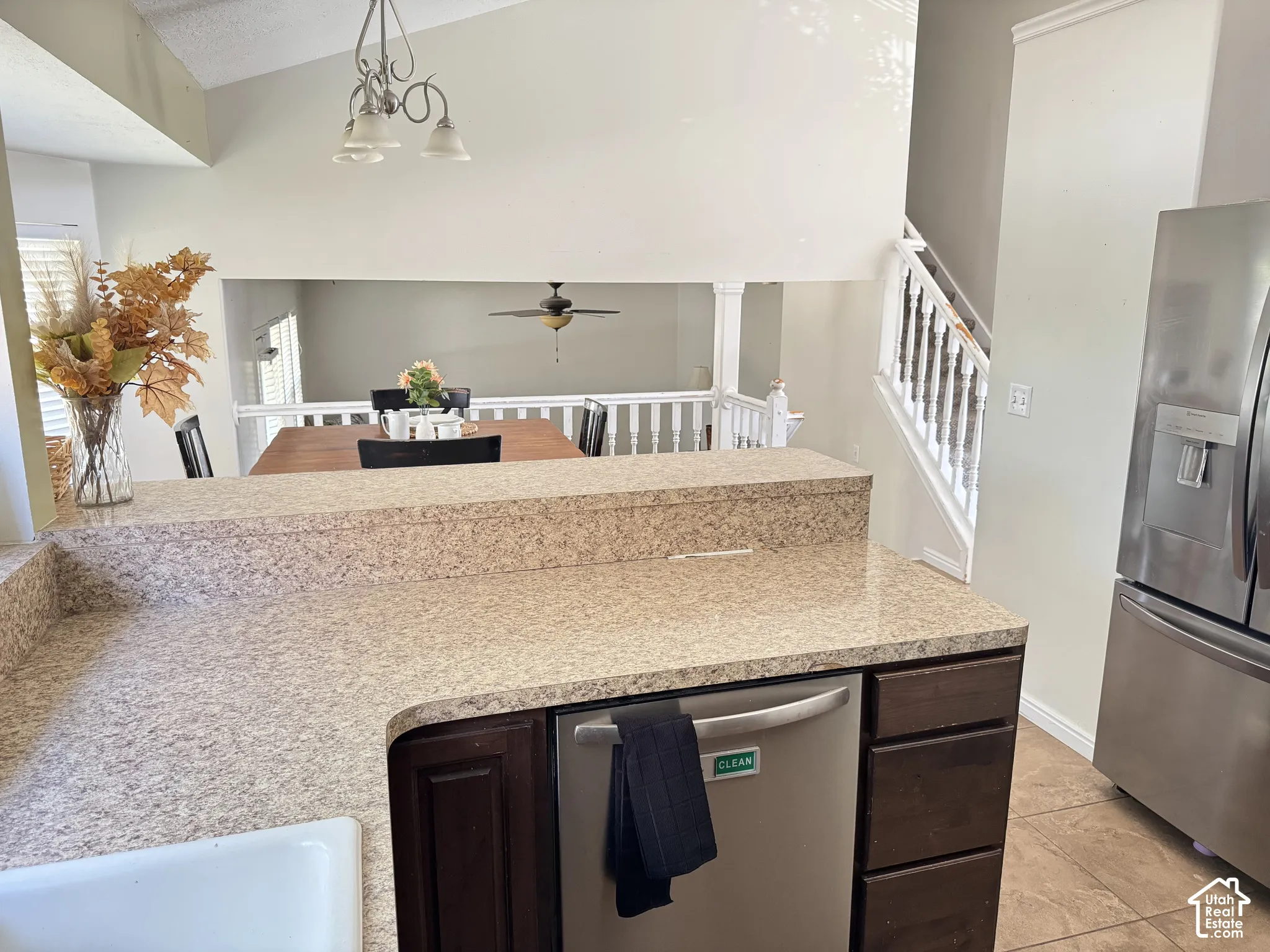 Kitchen featuring stone-finish countertops, stainless steel appliances, dark wood cabinetry, and vaulted ceilings with a three-light chandelier