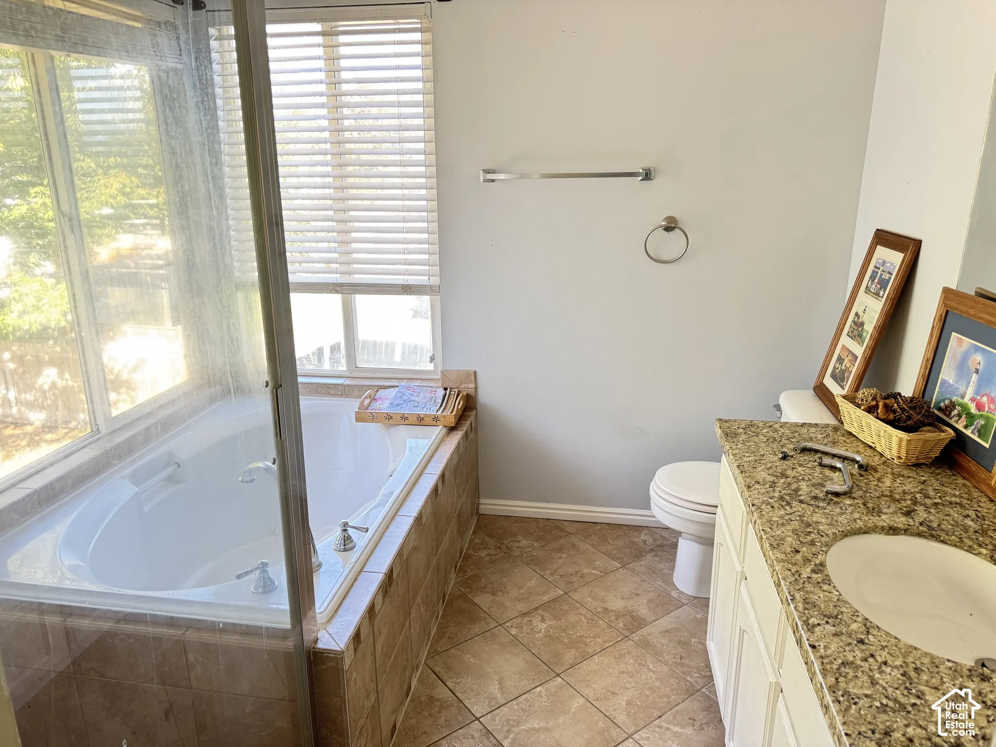 Soaking tub with tile surround, vanity featuring a stone-composite countertop and integrated sink, and ceramic tile flooring