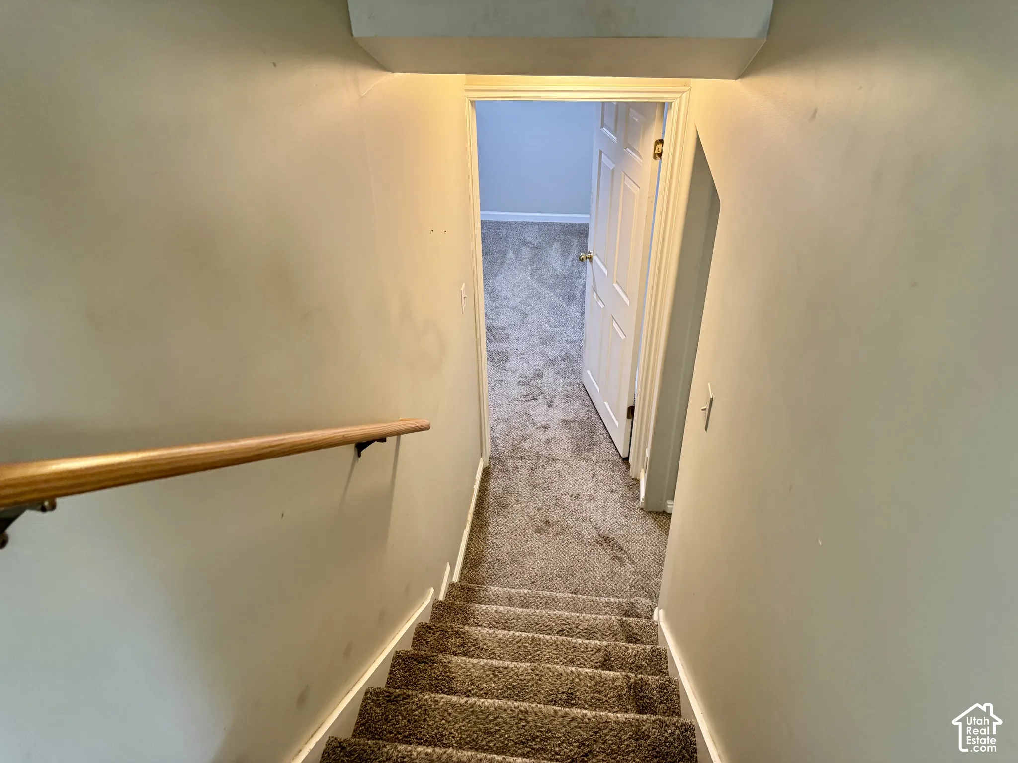 Staircase featuring neutral carpeting and a wall-mounted wood handrail with dark metal brackets, leading to an interior space with a six-panel door