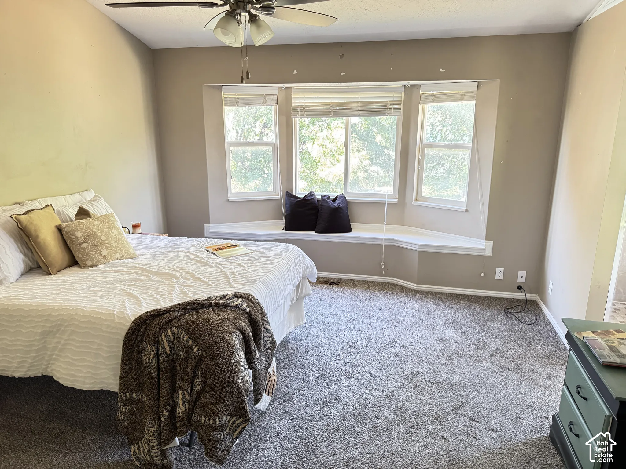 Room featuring a bay window with a built-in bench seat, neutral wall paint, carpeted flooring, and a ceiling fan with integrated lighting