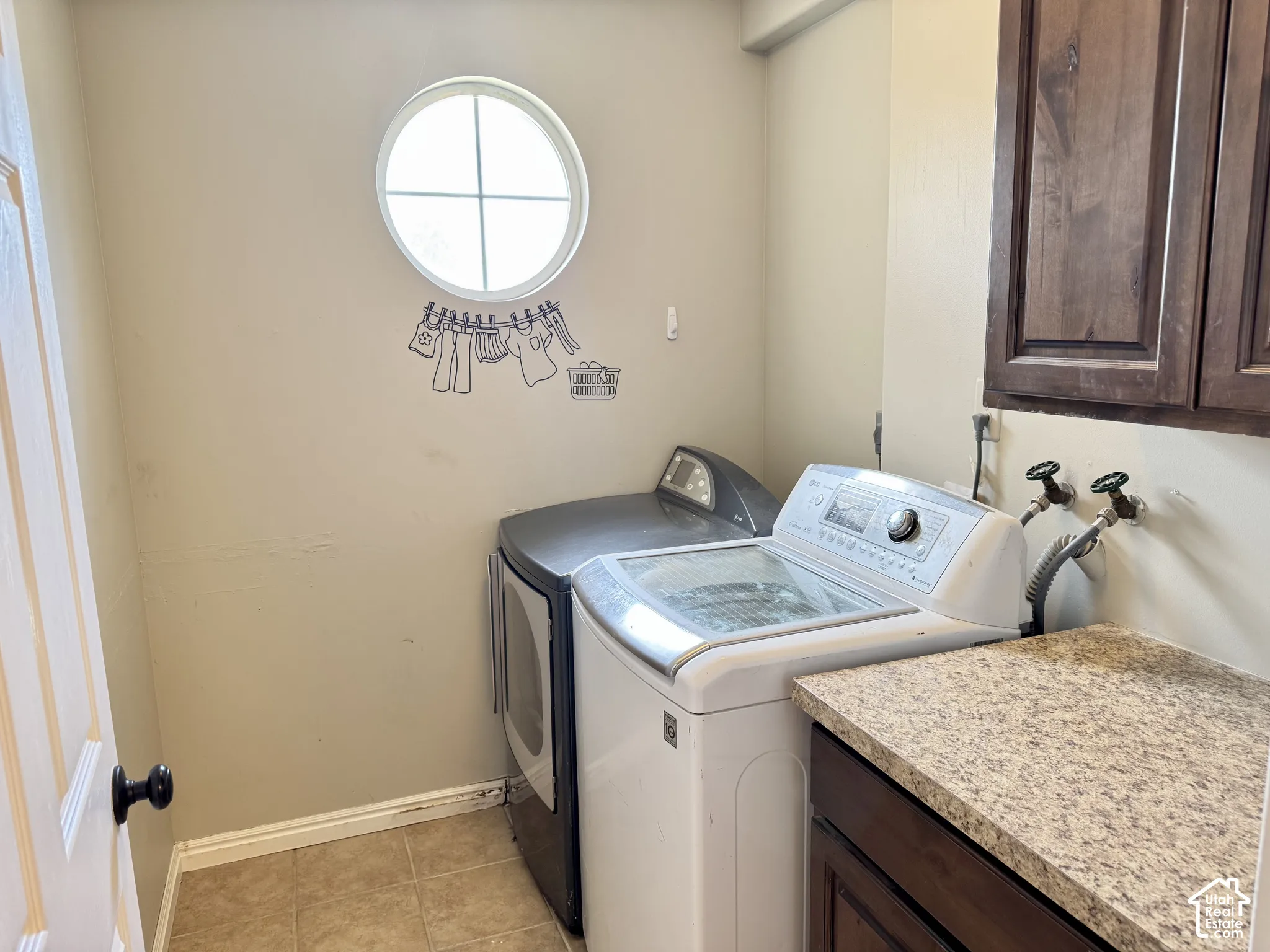 Laundry area featuring built-in dark wood cabinetry, laminate countertops, a circular accent window, and ceramic tile flooring