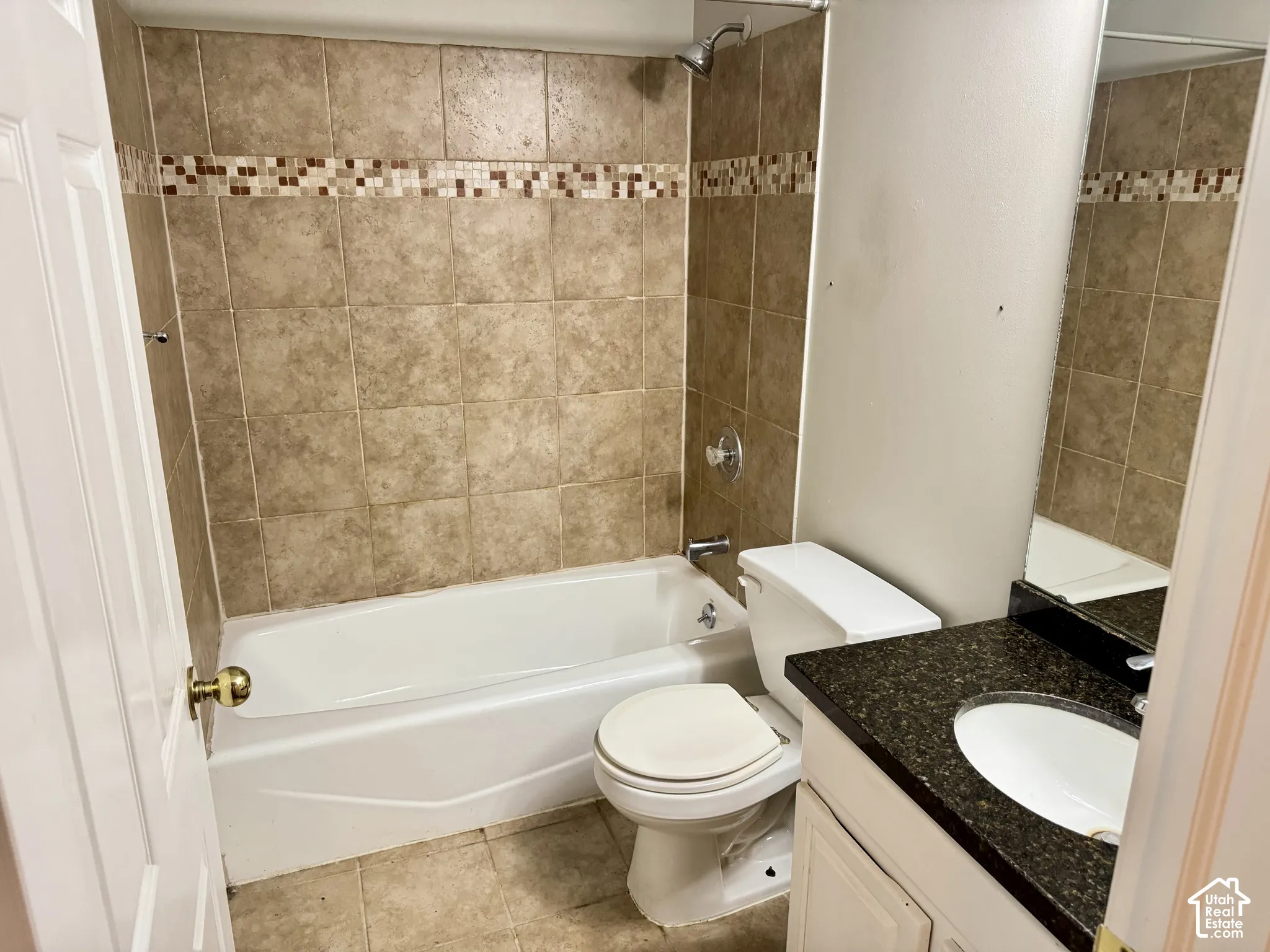 Bathroom featuring a tub-shower combination with tile surround and decorative glass mosaic inlay, dark stone-finish countertop, white oval undermount sink, and white vanity cabinetry