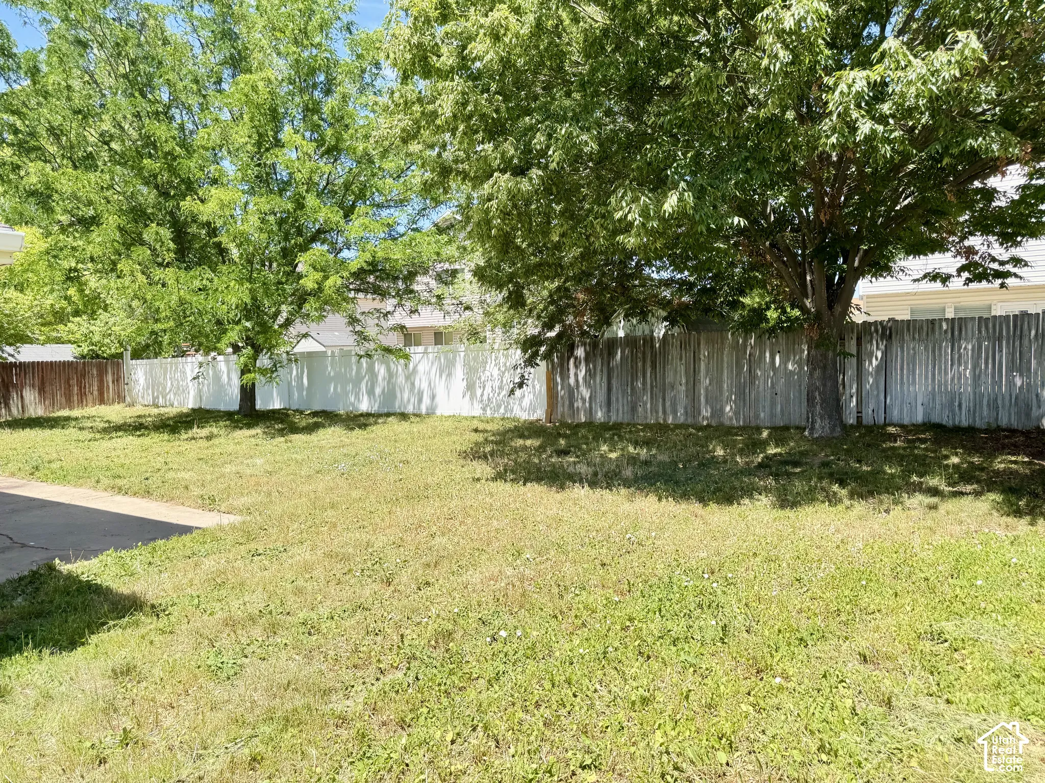 Backyard featuring a grass lawn, concrete patio, mature trees, and perimeter fencing