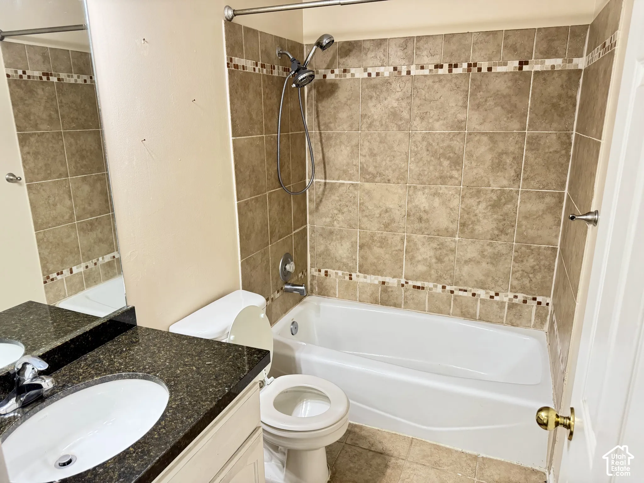 Bathroom featuring a dark stone-finish countertop, undermount sink, porcelain tub, and shower surround with neutral tile and decorative mosaic accent banding