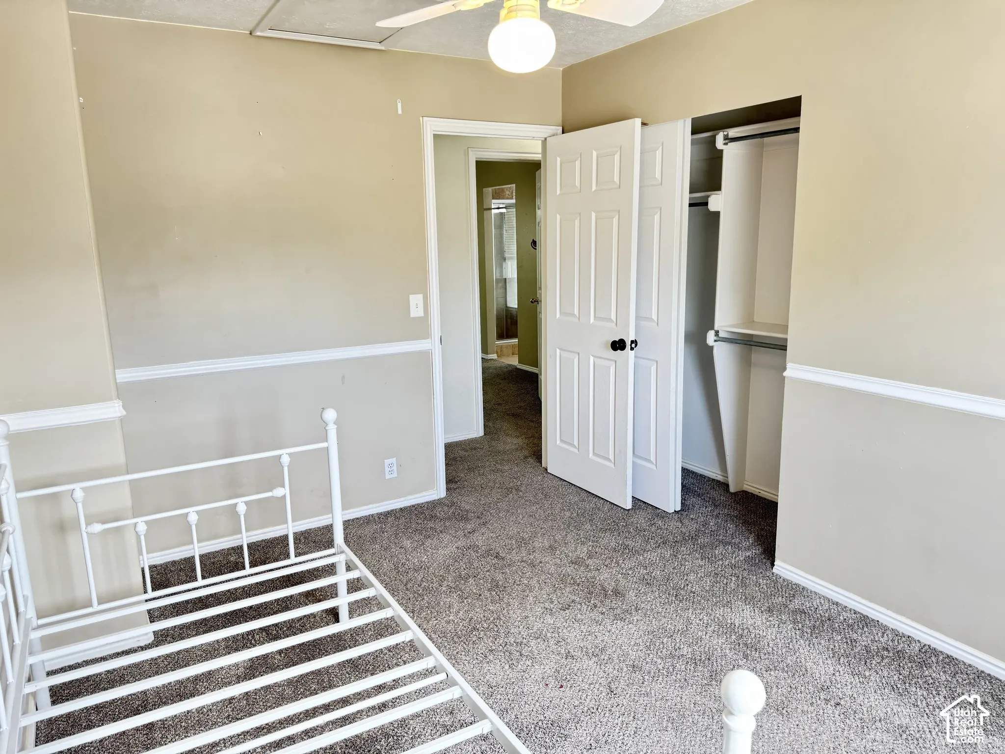 Room featuring neutral wall paint, white chair rail molding, carpeted flooring, a ceiling fan with light fixture, and a closet with double doors and built-in shelving