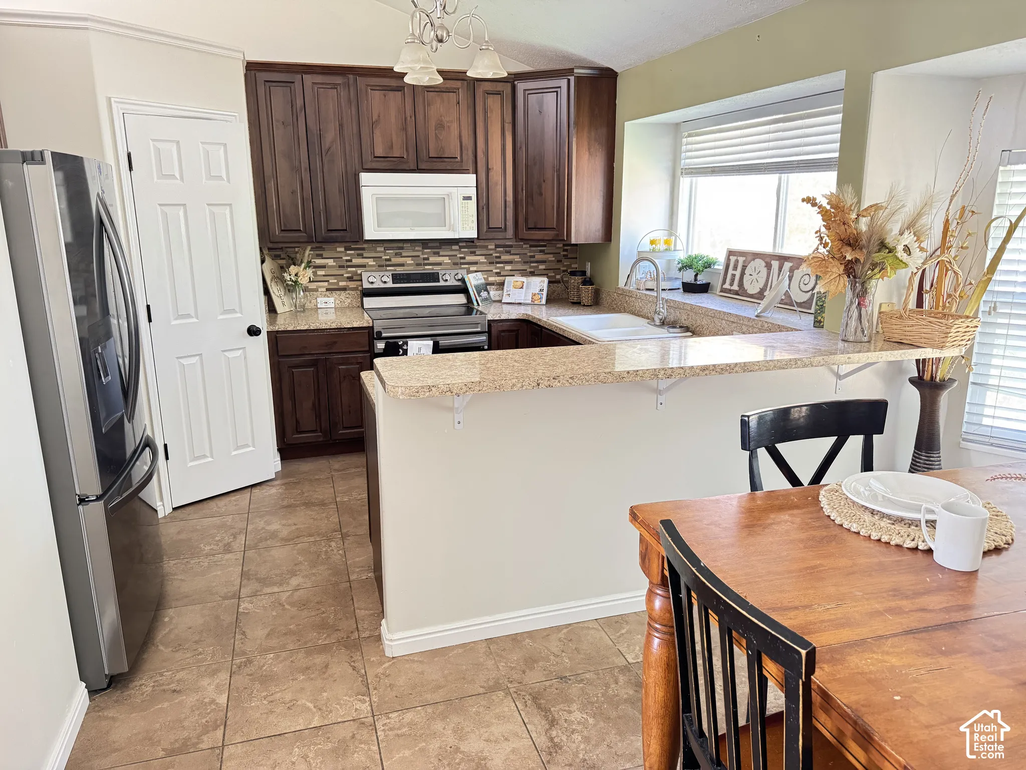 Kitchen featuring dark-finish cabinetry, stone-texture countertops, tile flooring, a tiled backsplash, and an extended breakfast bar