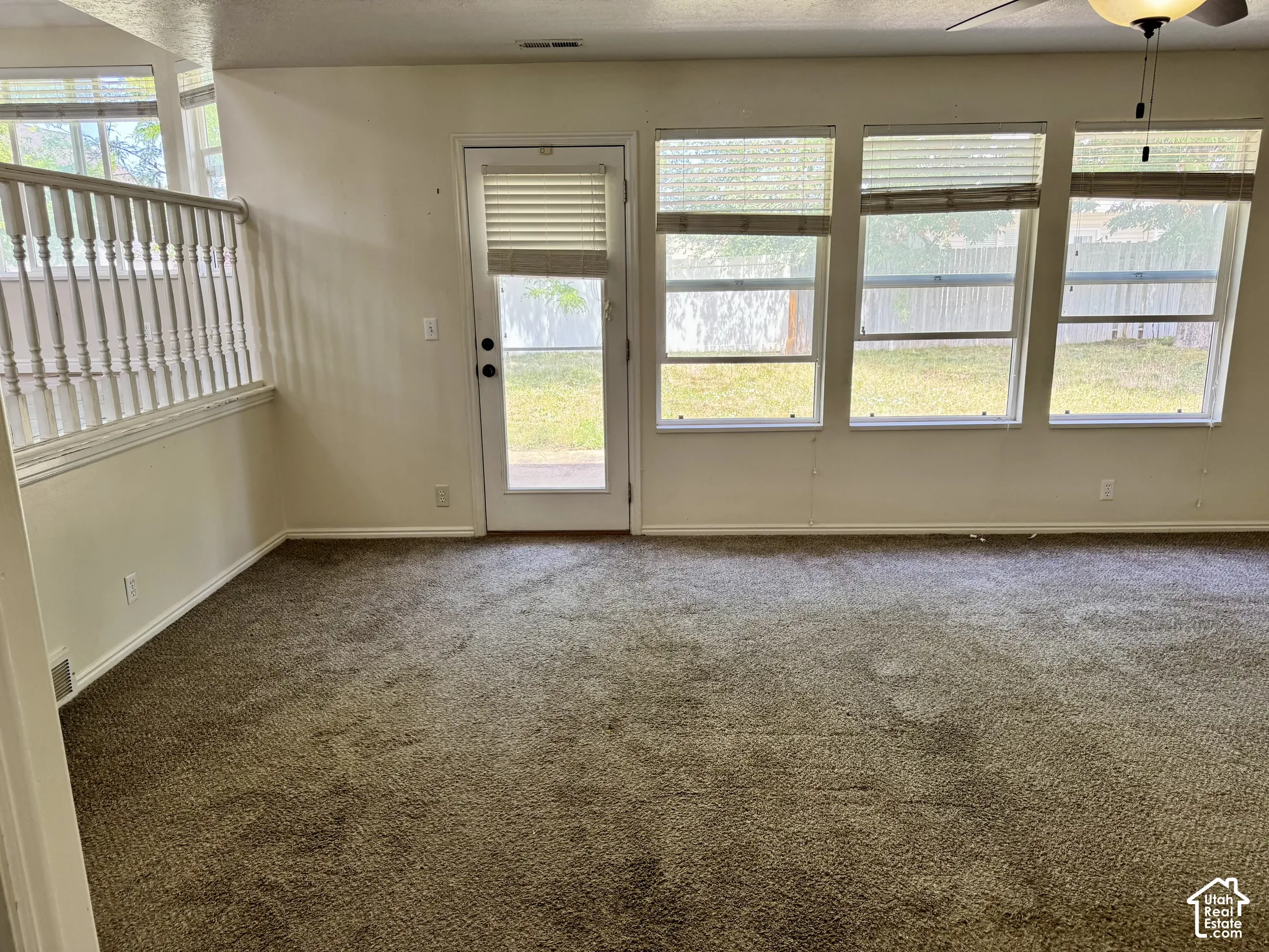 Interior featuring three large windows, a glass-panel exterior door, neutral carpeting, and a white wooden stair railing