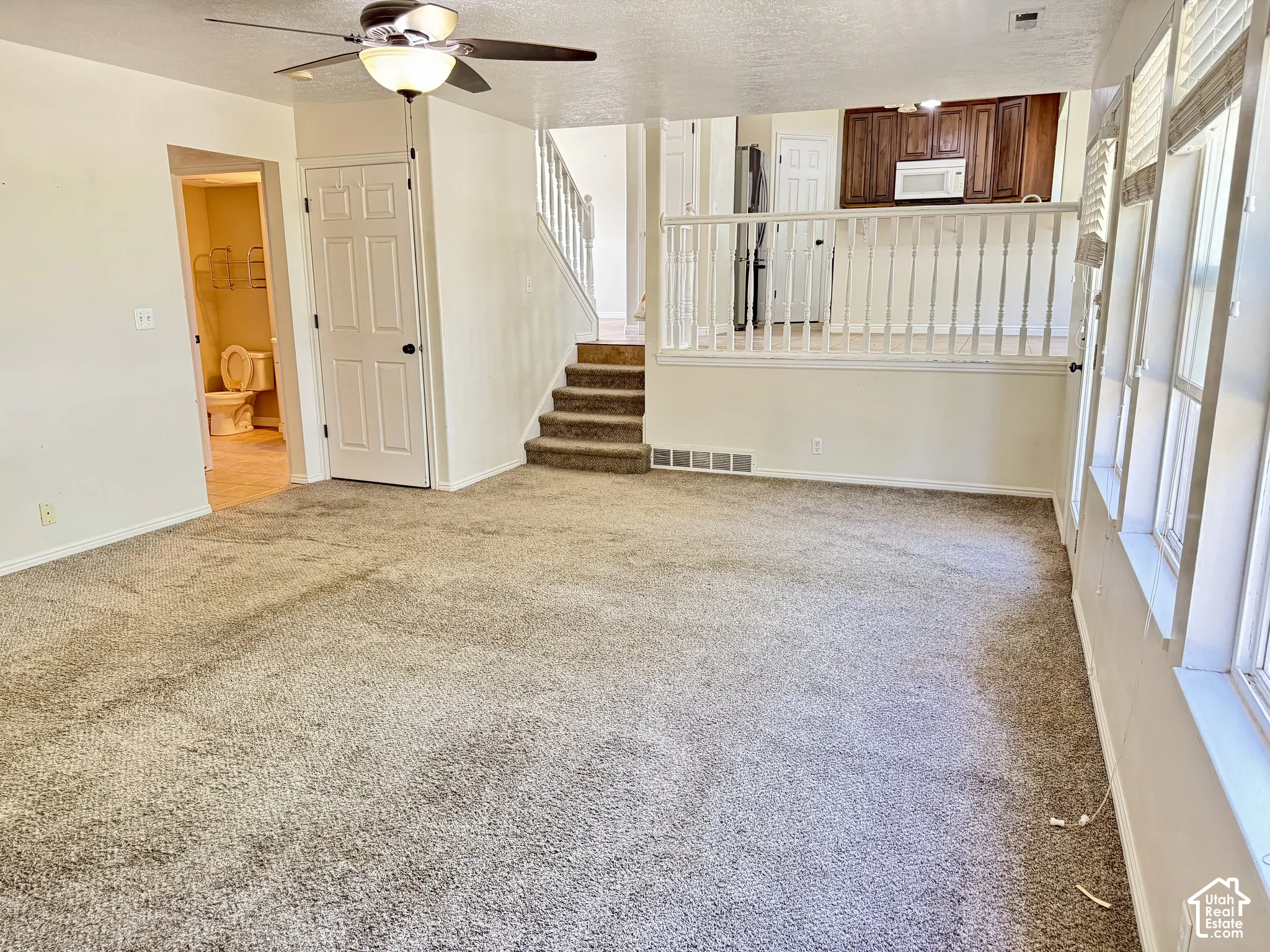 Multi-level interior featuring carpeting, a ceiling fan with integrated lighting, a staircase with a wooden balustrade, and a raised platform area with dark wood-finish cabinetry