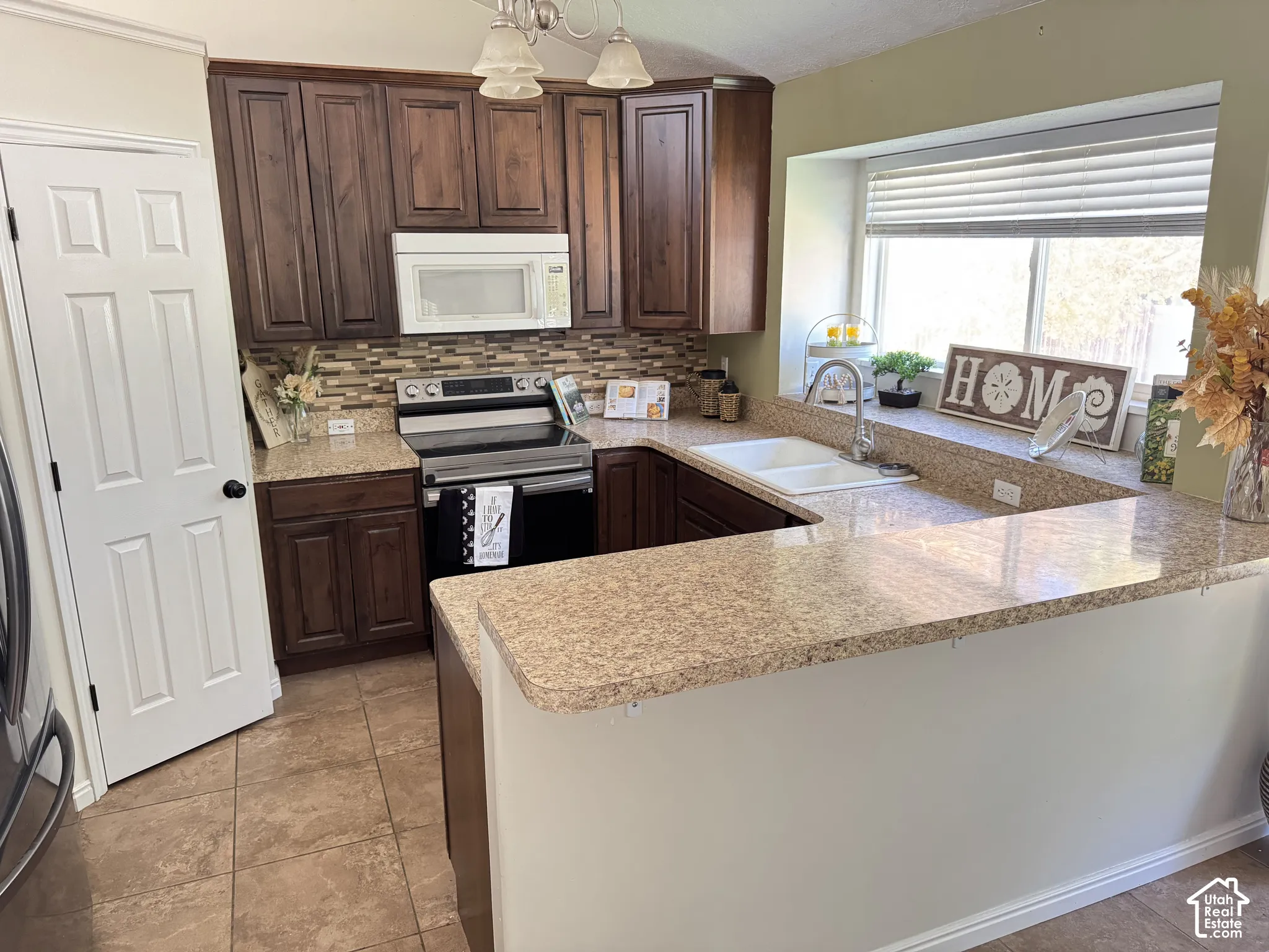 Kitchen featuring dark wood cabinetry, a decorative tile backsplash, stone-finish countertops, tile flooring, and a double-basin sink