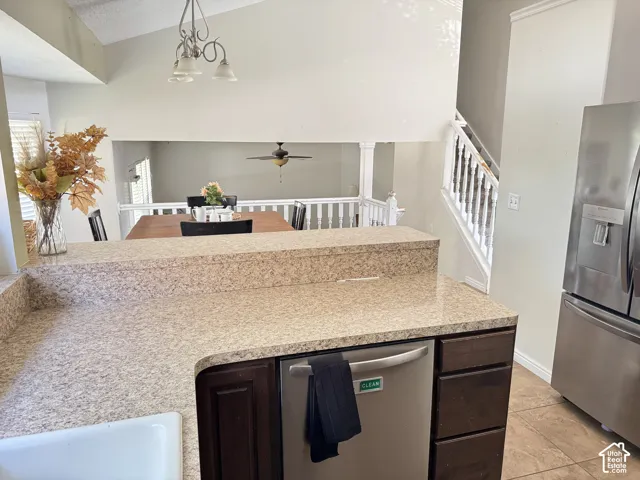 Kitchen featuring stone-finish countertops, stainless steel appliances, dark wood cabinetry, and vaulted ceilings with a three-light chandelier