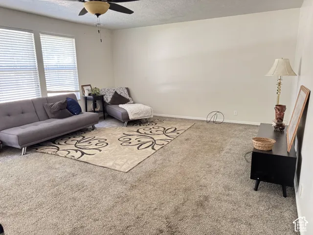 Spacious room featuring neutral carpeting, high-reaching walls, dual-pane windows with horizontal blinds, and a mounted ceiling fan with integrated lighting