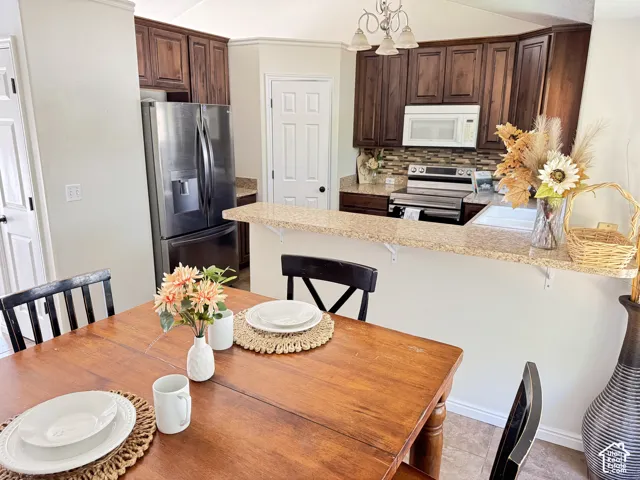 Kitchen featuring dark wood cabinetry, a stone-finish countertop peninsula, mosaic tile backsplash, and stainless steel appliances including a French-door refrigerator and built-in microwave