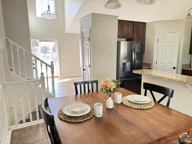Vaulted ceilings, kitchen breakfast bar with stone-finish countertops, dark wood cabinetry, stainless steel refrigerator, and white painted staircase railing