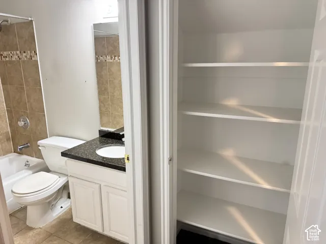 Bathroom featuring a vanity with dark stone countertop and integrated sink, tub-shower combination with tile surround, and an integrated storage closet with tiered shelving