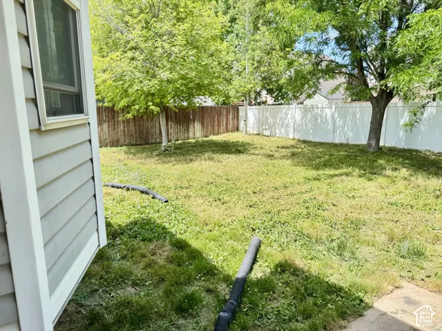Backyard featuring grey siding, a white vinyl perimeter fence, wood-tone privacy fencing, and mature trees