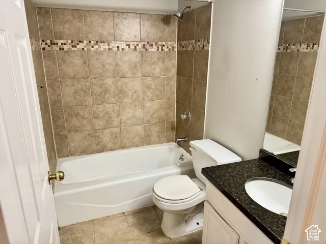 Bathroom featuring a tub-shower combination with tile surround and decorative glass mosaic inlay, dark stone-finish countertop, white oval undermount sink, and white vanity cabinetry