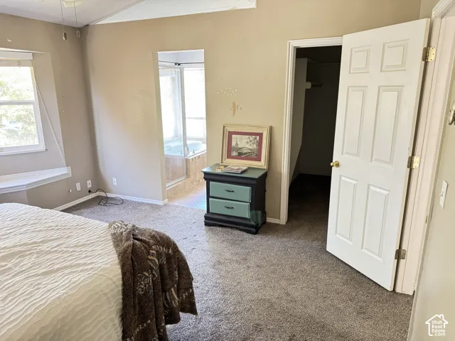Room featuring neutral carpeting, a large bay window with a ledge, vaulted ceilings, a walk-in closet, and a tiled soaking tub