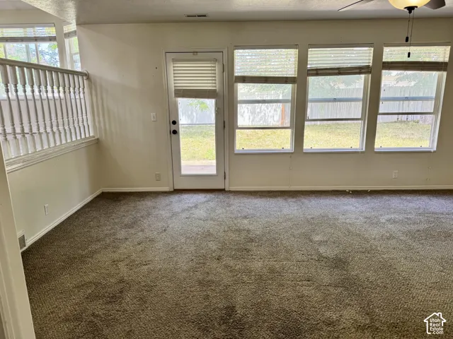 Interior featuring three large windows, a glass-panel exterior door, neutral carpeting, and a white wooden stair railing