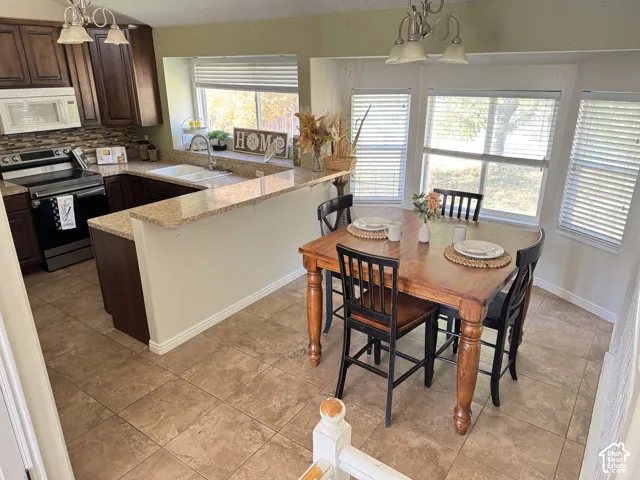 Kitchen featuring dark-finish cabinetry, stone-patterned countertops, a dual-basin sink, tile flooring, and a bay window