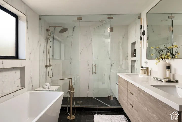 Bathroom featuring a dual-sink floating vanity with quartz countertops, a glass-enclosed walk-in shower with stone-finish tile surrounds, and a freestanding soaking tub with floor-mounted brass-finish hardware