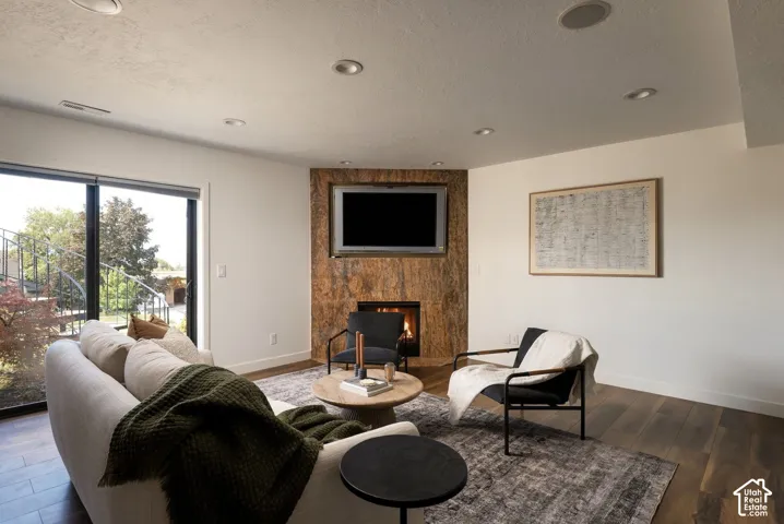 Living area featuring wood-finish flooring, recessed lighting, and a corner fireplace with a textured stone-finish surround