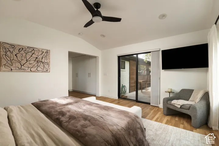 Vaulted ceilings with a matte black ceiling fan, wood-finish flooring, built-in floor-to-ceiling cabinetry, and sliding glass doors opening to an exterior concrete patio
