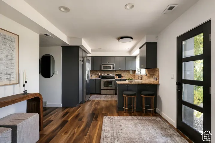 Kitchen featuring dark cabinetry, stone countertops, stainless steel appliances, and wood-finish flooring, complemented by a multi-panel glass entry door