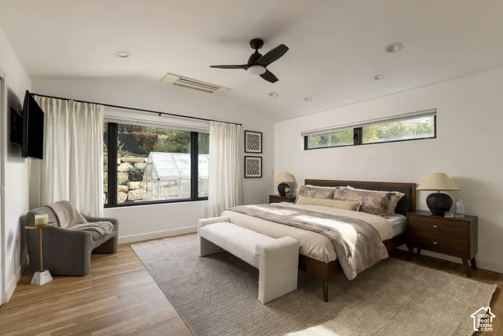 Vaulted ceiling with integrated recessed lighting and a matte black ceiling fan, expansive window featuring black trim, horizontal clerestory window, and light-tone wood-finish flooring