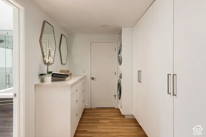 Custom cabinetry with integrated laundry appliances, wood-finish flooring, stone-surfaced countertop, and dual geometric mirrors
