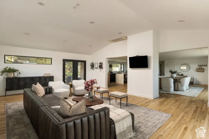 Open-concept interior featuring vaulted ceilings, recessed lighting, wood-finish flooring, and black-framed French doors