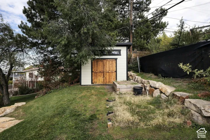 Exterior storage structure featuring horizontal siding, double wood doors, clerestory windows, and a stacked stone retaining wall