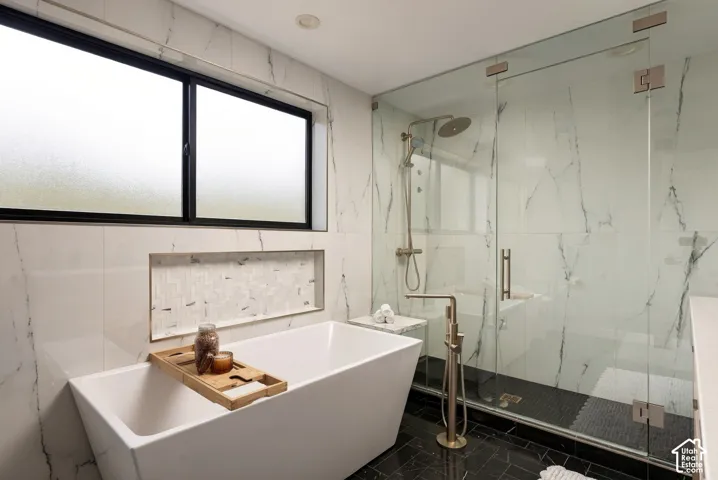 Freestanding soaking tub with floor-mounted faucet, frameless glass-enclosed shower, large-format tile surround, recessed wall niche, and black tile flooring