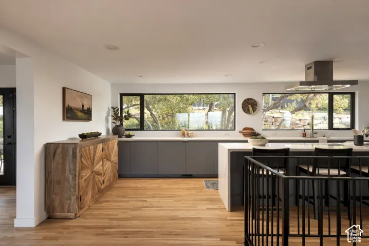 Modern kitchen featuring expansive horizontal windows, flat-panel cabinetry, a central island with a solid-surface countertop, a stainless steel range hood, and wood-finish flooring