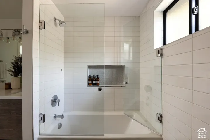 Shower and tub combination featuring rectangular white wall tiling, a frameless glass door, a recessed tiled storage niche, and polished chrome fixtures