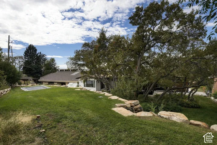 Sprawling backyard featuring tiered natural stone landscaping, mature shade trees, and a spacious lawn