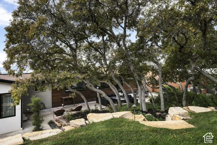 Exterior landscape featuring mature trees, terraced natural stone retaining walls, and a concrete patio