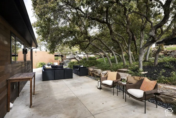 Concrete patio featuring tiered natural stone retaining walls, dark wood-tone horizontal exterior siding, and mature trees