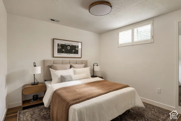 Room featuring white walls, wood-finish flooring, a flush-mount circular ceiling light, and a window with white shutters