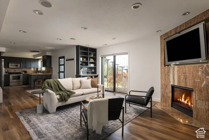 Fireplace with floor-to-ceiling stone surround, wood-finish flooring, recessed lighting, built-in shelving, and sliding glass door