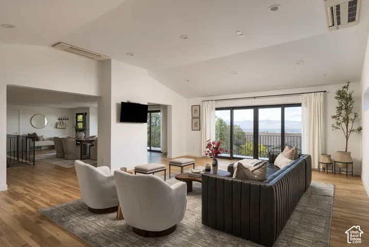 Vaulted ceilings with recessed lighting, wood-finish flooring, and expansive multi-panel sliding glass doors opening to a balcony with mountain scenery