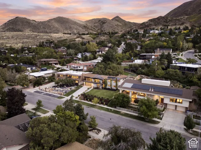 Aerial perspective featuring residential properties with integrated solar energy systems, multi-car garages, manicured landscaping, and mountain backdrops
