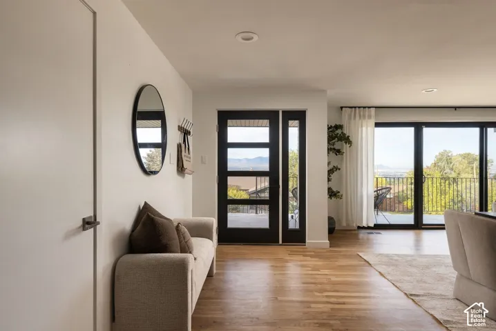 Entryway featuring wood-finish flooring, a contemporary multi-paneled front door with sidelight, recessed ceiling lighting, and floor-to-ceiling sliding glass doors
