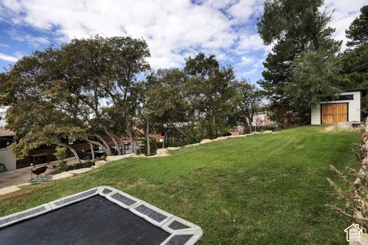 Expansive backyard featuring tiered landscaping, natural stone retaining walls, mature oak trees, and a detached structure with wood-finish double doors