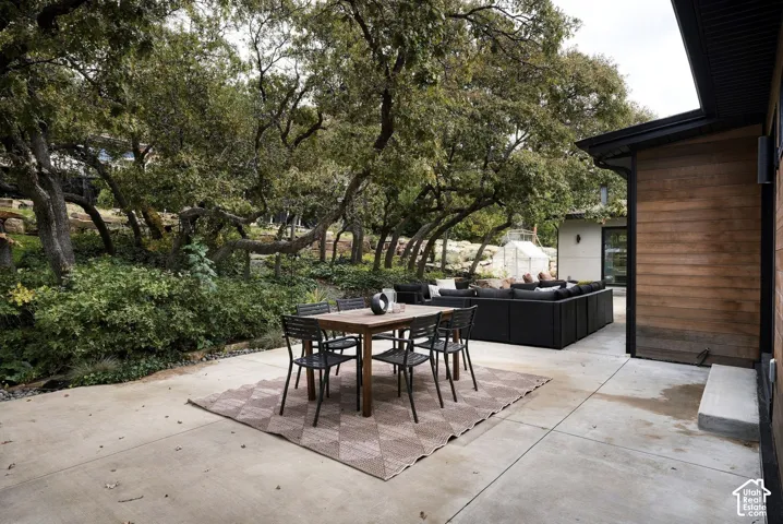 Concrete patio featuring horizontal wood siding, mature trees, and tiered landscaping