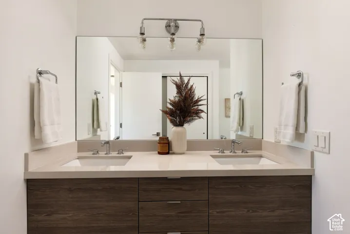 Dual-sink vanity featuring a quartz countertop, wood-finish cabinetry, a large frameless mirror, and chrome fixtures