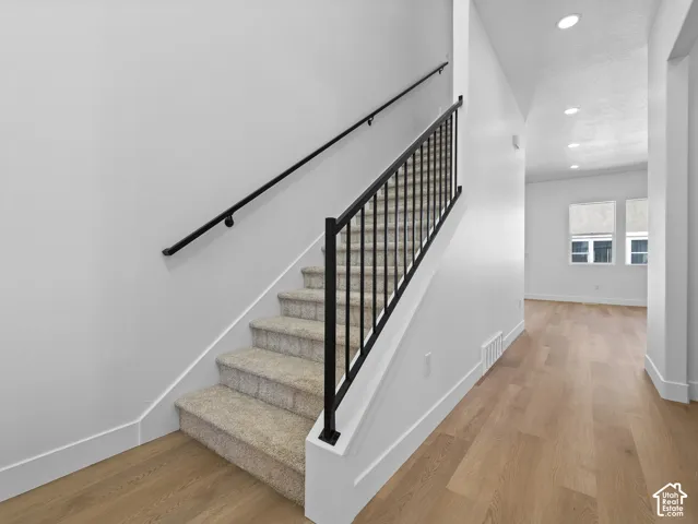 Staircase featuring carpeted treads, matte black metal railings, wood-finish flooring, and recessed ceiling lighting