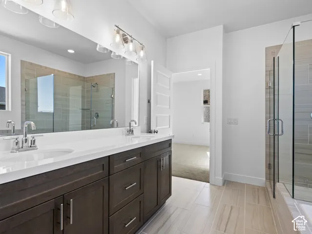 Dual-sink vanity with white countertops, dark wood-finish cabinetry, full-width wall mirror, and walk-in shower with floor-to-ceiling tile surround