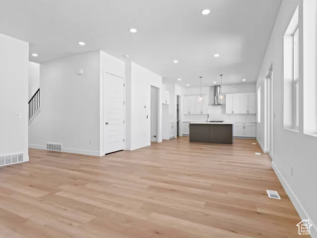 Open-concept interior featuring wood-finish flooring, recessed lighting, a contrasting center island, white cabinetry, and stainless steel range hood